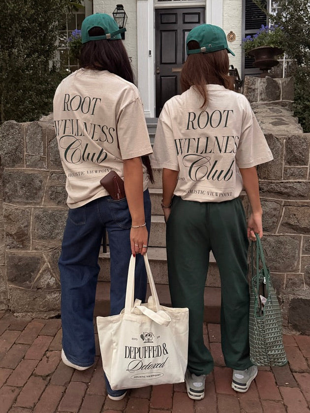 Two people wearing 'ROOT WELLNESS Club' shirts standing in front of a house.