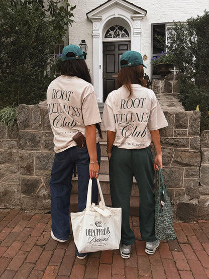 Two people wearing 'ROOT WELLNESS Club' shirts standing in front of a house.
