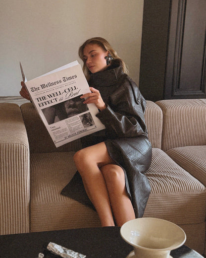 Woman reading a newspaper on a couch in a cozy living room.