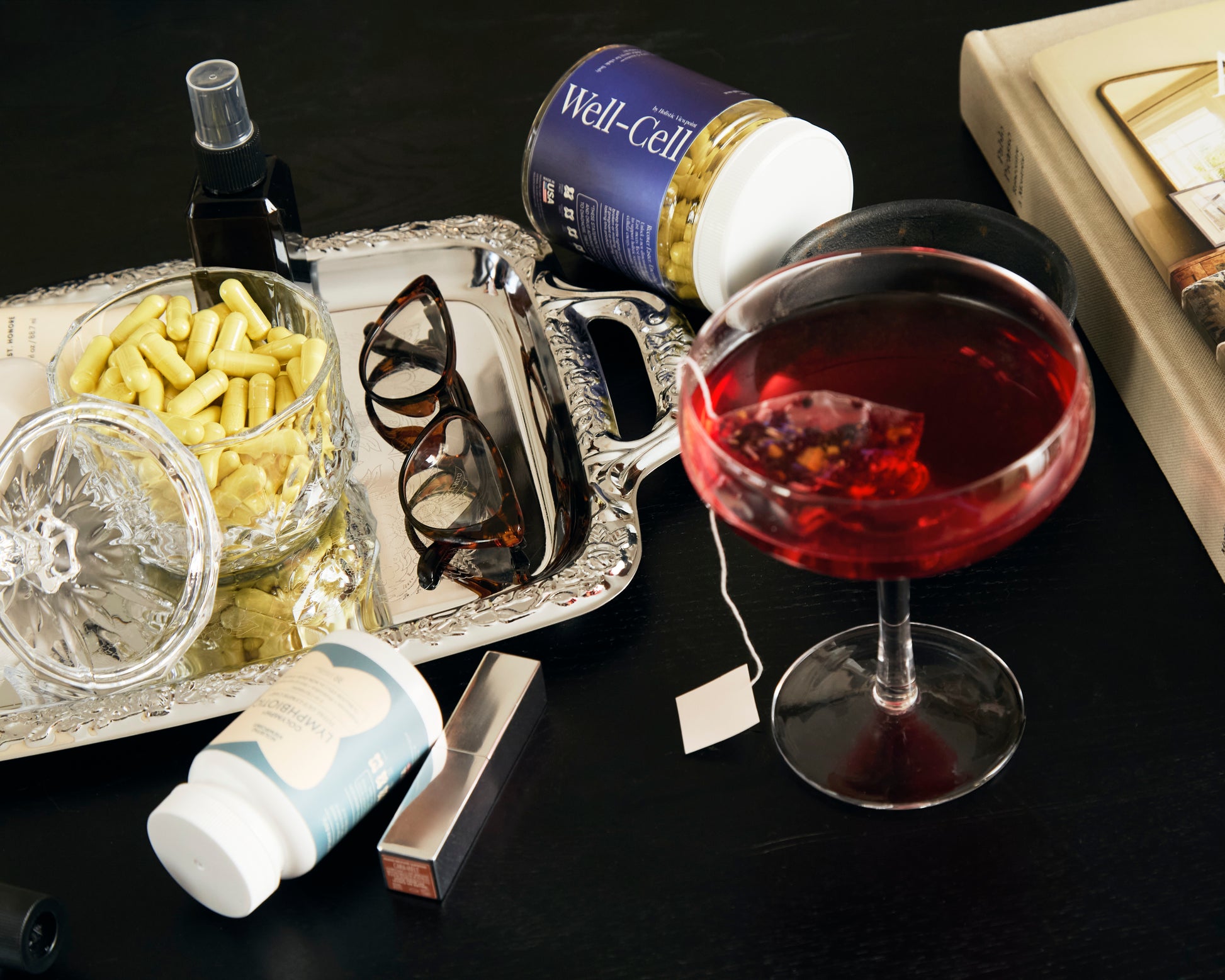 Tray with wine glass, pills, and other items on a dark surface